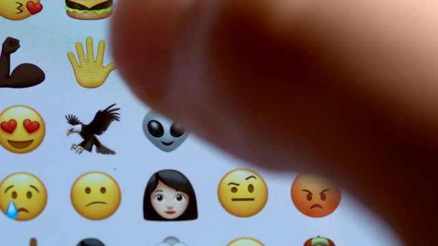 This closeup POV macro video shows fingers pressing and texting emojis on phone screen.