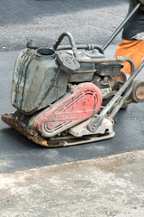 Road workers compact the asphalt with a vibrating rammer on the road. Worker with compactor at a road construction site. vertical photo