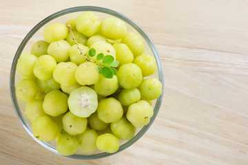 Star gooseberry with medicinal properties and sour fruit of thailand. Top view fresh phyllanthus acidus or star gooseberry with green leaves in cup glass on wood table.