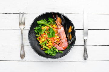 Seafood with vegetables. Boiled vegetables with shrimp and mussels. In a black plate. Top view. Free copy space.