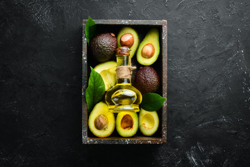 Avocado oil and fresh avocados on a black background. Rustic style. Top view. Free space for your text.