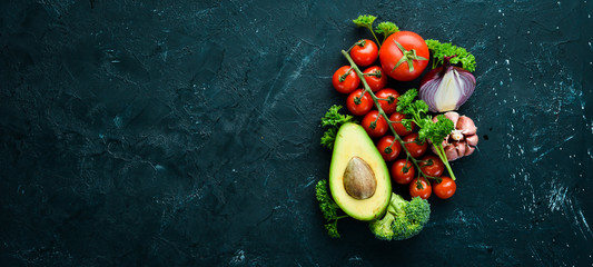 Fresh vegetables on a black background. Avocados, tomatoes, garlic, parsley, paprika. Top view....