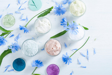 moisturizers, bath salts and powder compacts with blue chicory flowers on white wood table
