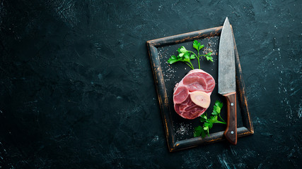 Raw fresh cross cut veal shank for making Osso Buco with spices and herbs on a black background. Top view. Free space for your text.