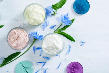 moisturizers, bath salts and powder compacts with blue chicory flowers on white wood table