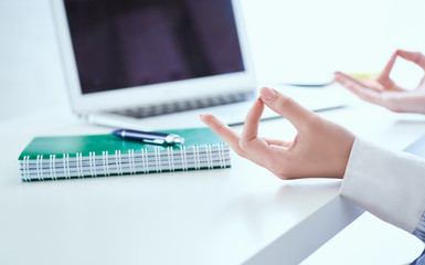Calm businesswoman meditating at work, focus on female hands in mudra, close up view. Peaceful mindful employee practicing exercises at workplace.