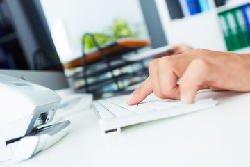 Hands of a young businessman typing on a keyboard while working on a desktop computer at the office space.