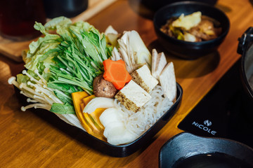 Sukiyaki vegetables set including cabbage, false pak choi, carrot, shiitake, enokitake, tofu, pumpkin, scallion and konjac noodle in black plate.