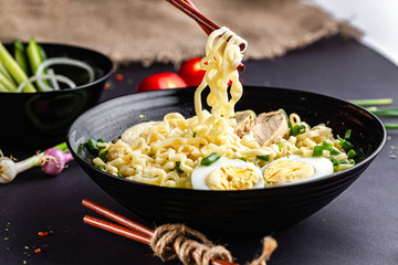 Japanese ramen soup with chicken, egg, chives in black bowl on dark background.