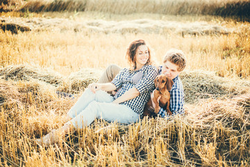 Naklejka na ściany i meble Couple with dog sitting in a field and having a fun on a warm summer day.