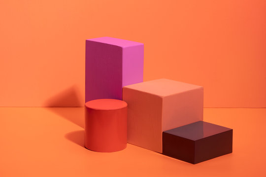 Geometric shapes in different colors on orange background. Three-dimensional solid figures on colored paper.