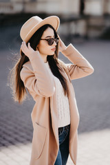 Young stylish beautiful woman walking in street, wearing coat and sunglasses, fashion outfit.