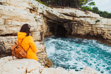 Fototapeta premium young woman sitting at cliff looking at grotto cave with blue azure water