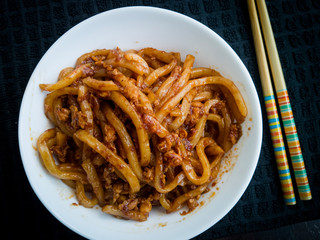 Asian fried noodles with soy sauce and eggs in a bowl. Black background. Closeup. Top view. Udon noodles and  chopsticks. Asian style dinner/lunch. Chinese/Japanese noodles
