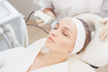 Obraz na płótnie Canvas Close-up cosmetologist making ultrasound hardware cleaning of the face of her patient a beautiful young woman. Concept skin cleansing and restoration of elasticity