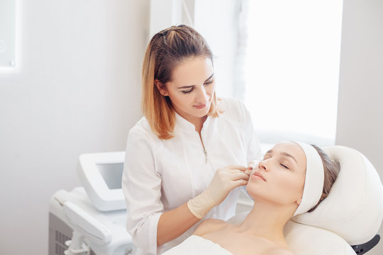 Female cosmetologist makes beauty shots to her client woman sitting on a couch. Concept of rejuvenating aesthetic salon procedures