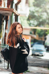 Candid portrait of young beautiful long hair girl fashion model hipster in black hoodie on city street