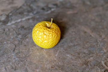 Wrinkled yellow old apple lies on the table top.