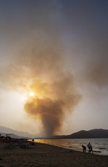 Obraz premium Smoke from a large fire billows into the sky as the sun sets, beach