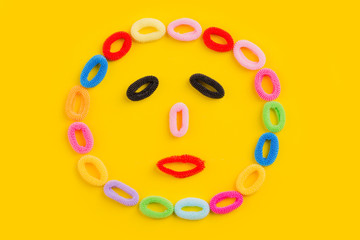Face laid out from scrunchy. Colored hair ties on a yellow background.