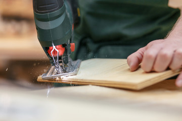 Unidentified male carpenter jigsaw out the base for a skateboard. Concept of a professional workshop for wood processing