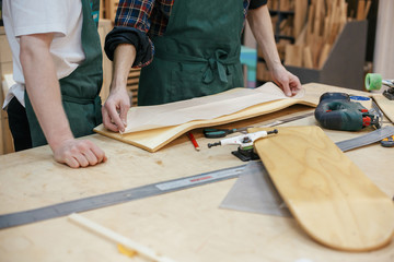 Hands of the master carpenter pressed against the board mold to cut a skateboard from a wooden board. Concept of creating exclusive wooden products on order