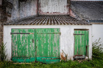 abandoned french farmhouse with green wooden painted doors in disrepair and flaking