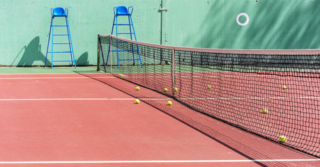 tennis court with hard coating, balls near net, two towers for referee, concrete wall background,...