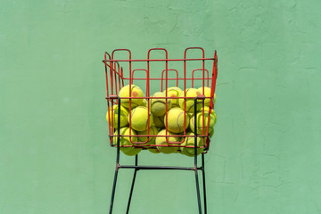 basket with yellow tennis balls for training and learning game of tennis, green concrete wall background