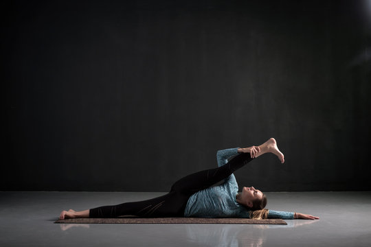 Young european woman doing yoga asana Anantasana or Side Reclining Leg Lift on black background