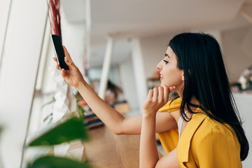 Attractive dark-haired young woman taking picture with phone camera. Work in coworking white room....