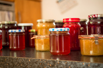 Jars of homemade marmelade stand on a kitchen top.