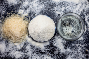 Rice water in a glass bowl along with rice grains & its powder also on wooden surface & some rice power spread on the surface for the treatment of various things such as Home Remedy,Beauty & Health.