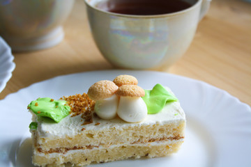 Cream cake on a white plate and a сup of tea in the background