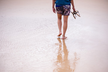 Woman holding her sandals in hand while walking on beach