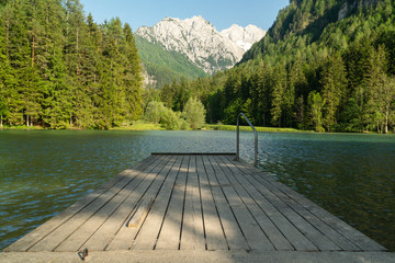 A scenic view of the alps taken at Jezersko lake, Slovenia. Scenic background and nice water reflection with wooden pier in the foreground.