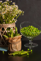 Beautiful summer still life with green peas and wildflowers on a black wooden table