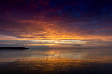 Sunset on the background of the water. Reflected orange and purple light on the clouds