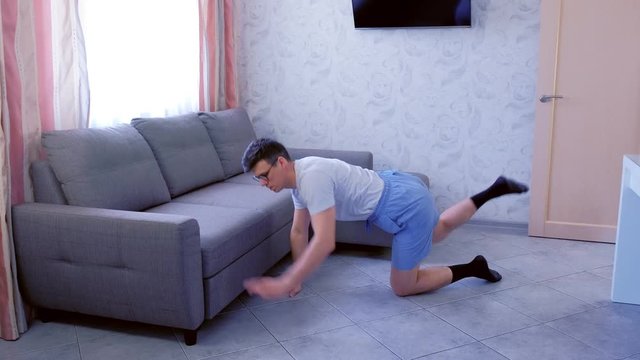 Funny nerd man in glasses and shorts is doing stretching fitness exercises standing on all fours at home. Sport humor concept.