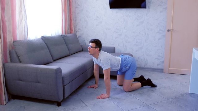 Funny nerd man in glasses and shorts is doing stretching exercise for back standing on all fours at home. Sport humor concept.