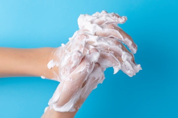 Teenager washes his hands with foam soap on a blue bright background