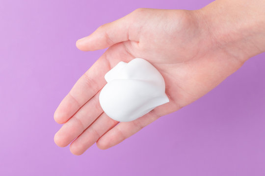 White shaving foam in the hand of a teenager on a blue bright background