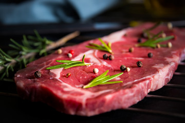 Raw beef meat, uncooked steak with rosemary, lemon and spices on black