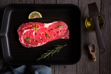 Raw beef meat, uncooked steak with rosemary, lemon and spices on black frying pan