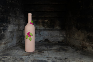 A hand-painted empty wine bottle with individual decorative design of flowers set in a blackened stone fireplace with copy space