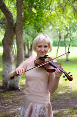 The Russian woman plays a violin in the park in the summer.
