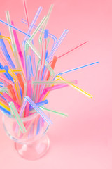 Multicolored plastic cocktail straws in an empty glass cup on a pink background. Concept: holiday, party, ecology, plastic