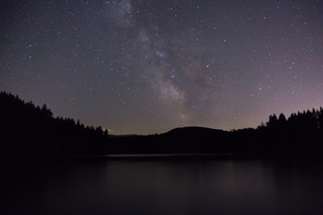 purple night sky stars over mountain lake. Milky way galaxy in summer starry night