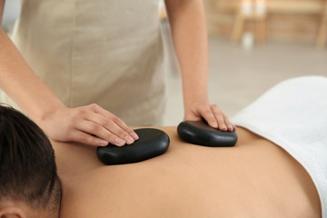 Man receiving hot stone massage in spa salon, closeup