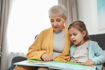 Fototapeta premium Cute girl and her grandmother reading book at home